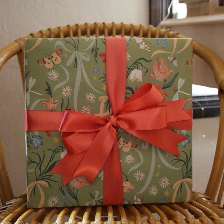 Gift box with floral pattern and red ribbon on a wicker chair