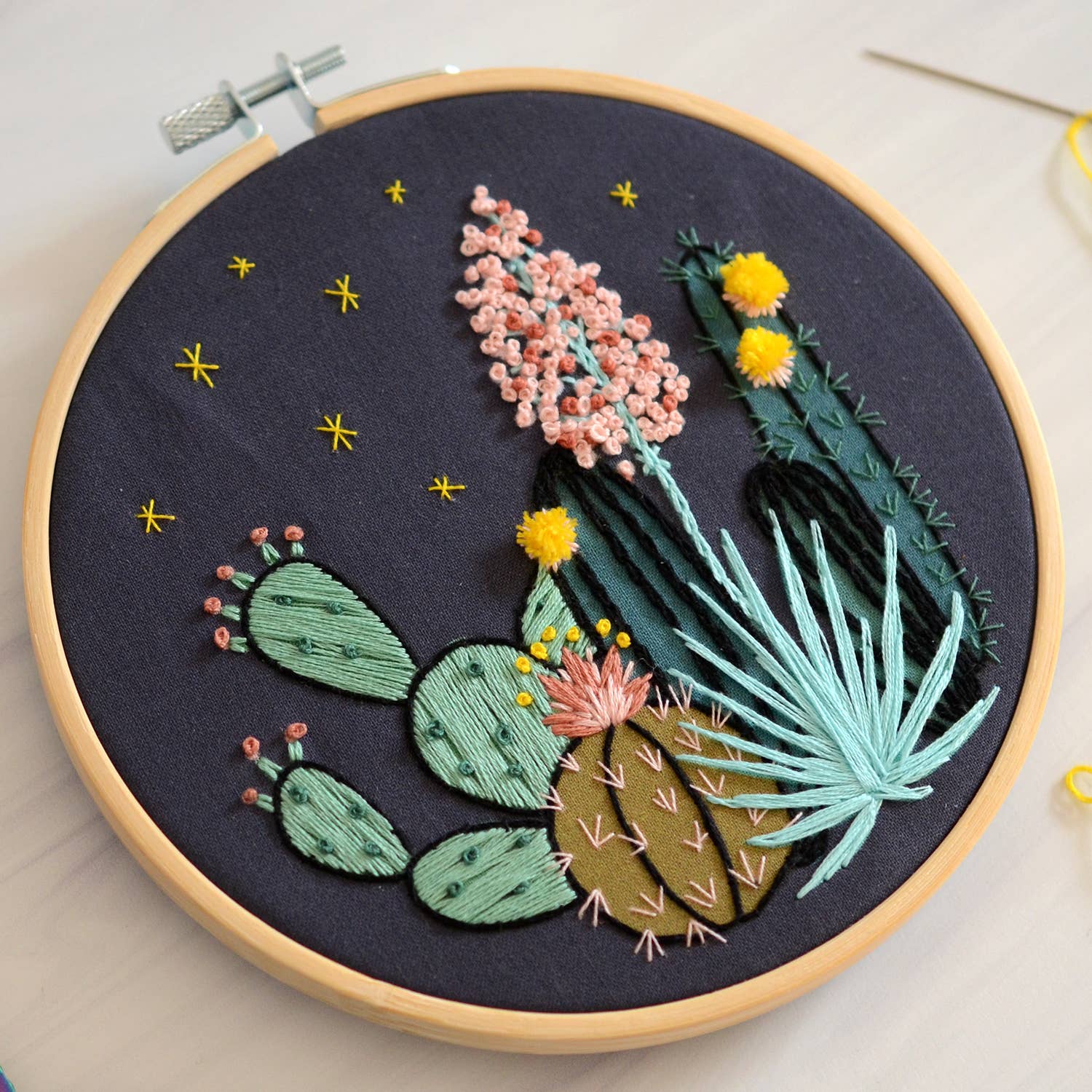 Embroidery hoop with embroidered cacti and flowers on a dark fabric background